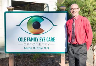 Aaron D. Cole O.D. standing next to a Cole Family Eye Care sign.